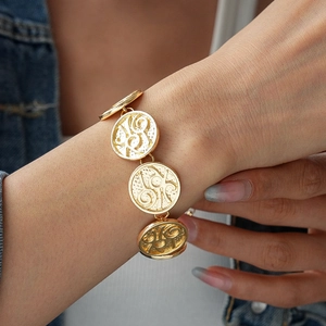 Close-up of gold vintage coin bracelet with embossed textures on a denim sleeve