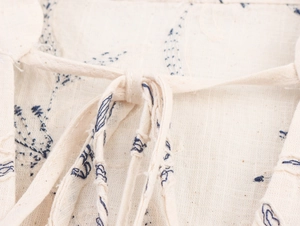 Detail of embroidered neckline on linen V-neck top with navy floral stitching and tassel ties
