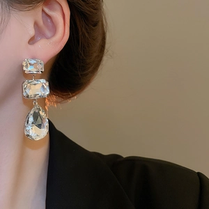 Detailed view of large three-tier crystal drop earrings with teardrop pendant on model