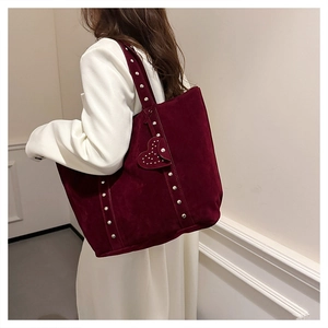 Close-up of deep red suede tote bag featuring metallic rivet details and heart pendant
