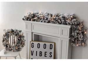 Detail of pre-lit flocked Christmas garland and wreath with pine cones and red berries