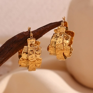Detail of 18K gold-plated oval earrings with lava texture on rustic wood stand