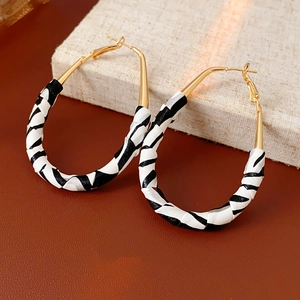 Détail de boucles d'oreilles dorées à motif zébré sur un présentoir en tissu neutre
