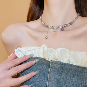 Close-up of beaded necklace with purple heart and frosted bear pendant on skin
