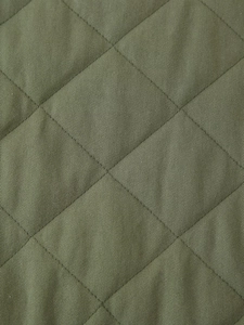 Macro shot of olive green quilted fabric with diamond stitch pattern on the jacket