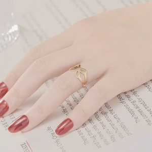 Close-up of a gold bow-shaped titanium steel ring on finger with red nail polish