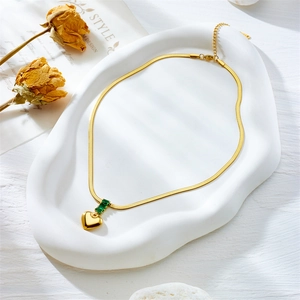 Retro gold snake chain necklace with green gem heart pendant on white plate