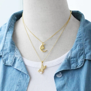 Detail of layered gold necklace featuring moon heart and bird charms with white pearl