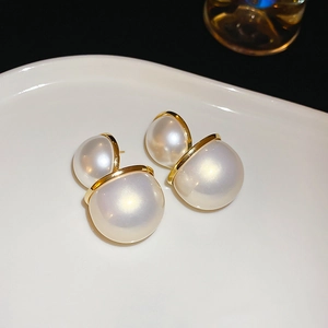Gros plan de boucles d'oreilles double perle avec bords dorés sur un plateau en céramique