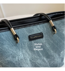 Detail of light blue denim tote bag featuring black leather trim and branded leather patch