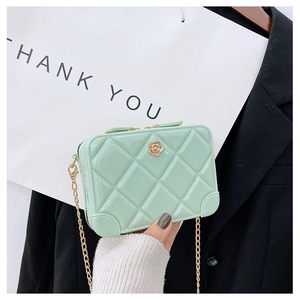 Macro shot of green diamond-quilted PVC jelly bag with golden flower clasp and chain