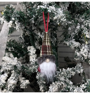 Close-up of a Christmas gnome hanging ornament with a dark plaid hat on a snowy pine tree
