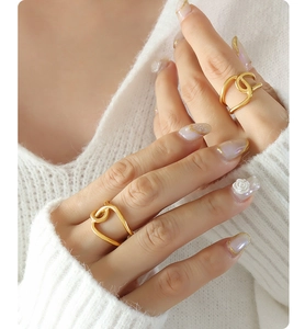 Close-up of golden interlocking rings on model finger over white knitwear
