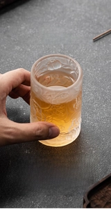 Frosted glass tea cup with embossed cat face and floral patterns in hand view