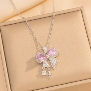 Close-up of silver bow necklace with pink heart crystals on a beige jewelry box