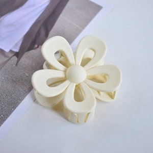 Top view of a creamy white flower hair claw clip on a clean surface with a magazine