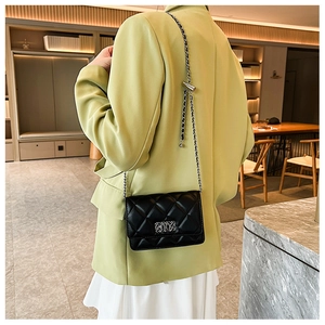 Detail of silver chain strap and metal clasp on black quilted small square crossbody bag