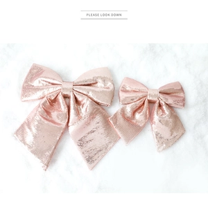 Close-up of rose gold sequin Christmas bows in two sizes on a white snowy surface