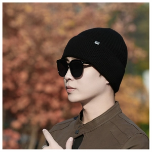 Detail of black ribbed knit beanie featuring a small metal logo tag on soft thick fabric