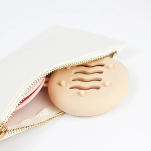 Beige silicone makeup sponge travel case with air holes being tucked into a white pouch