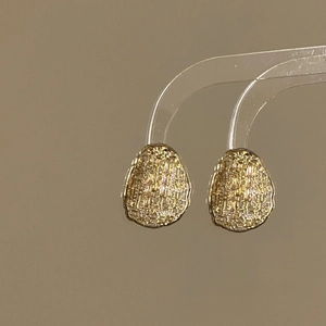 Close-up of gold-plated oval stud earrings featuring detailed textured pebble finish
