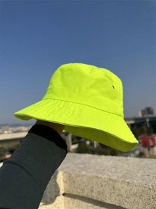 Neon yellow sun bucket hat held against a clear blue sky background in bright sunlight