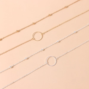 Golden and silver chain necklaces with ring pendants displayed on a warm beige background