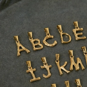 Polished 18K gold plated stainless steel 3D bamboo style alphabet charms on stone background