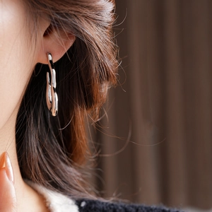 Close-up of a silver liquid metal earring with a fluid wavy design on a model ear