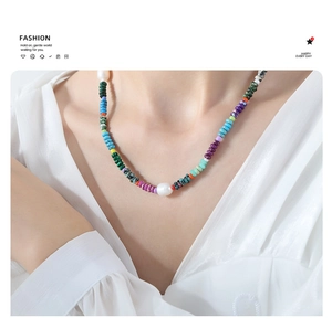 Close-up of a bohemian pearl and colorful stone bead necklace worn on a white shirt