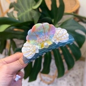 Shell shaped hair claw clip with gradient colors, pearls and rhinestones on a green background