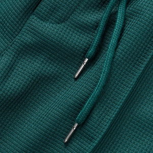 Detalle macro de tela de punto gofrado verde oscuro con cordón y punta metálica plata