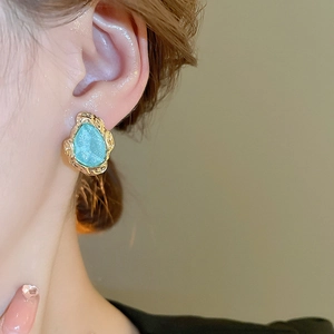 Close-up of vintage gold rimmed blue stone earrings worn by a model in a studio setting