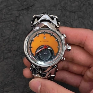 Silver metal watch with orange and black dial held against a dark textured background