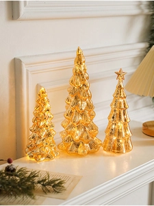 Three glowing gold glass Christmas tree ornaments with warm LED lights on a white mantel