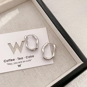 Sleek silver irregular geometric hoop earrings on a minimalist beige linen jewelry tray