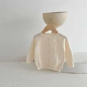 Vue détaillée du gilet en tricot ajouré pour bébé, texture crème douce, charmants boutons délicats.
