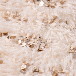 Detailaufnahme von flauschigem cremeweißem Kunstfell mit gold glänzenden Pailletten