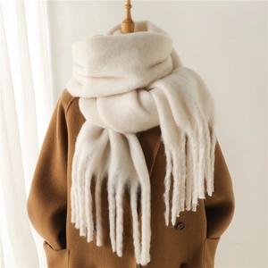 Gros plan d'une écharpe en mohair blanc crème avec de larges franges sur un manteau beige