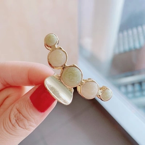 Close-up of golden claw clip featuring marbled light green and white decorative spheres