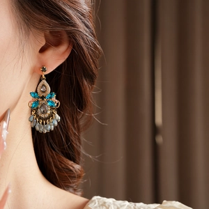 Close-up of bohemian gold earrings with blue crystals and beaded tassels worn by a model