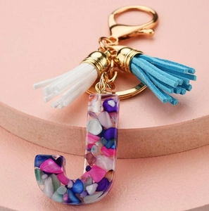 Detail of letter J keychain with colorful stone inlay and blue and white tassels