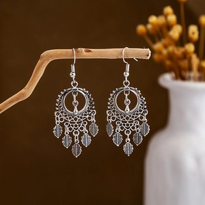 Close-up of vintage silver tassel earrings with leaf charms hanging on a wooden branch