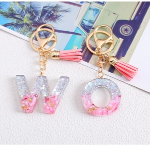 Detail of resin alphabet keychains with pink glitter, tassels, and gold metal hardware