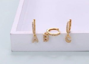 Macro detail of gold A B C letter earrings with sparkling cubic zirconia on a white stand
