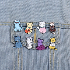 Detailed view of eight colorful enamel cat brooches pinned on a light blue denim jacket pocket