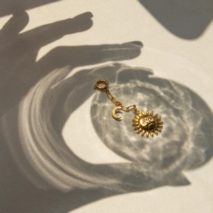 Artistic close-up of golden sun and moon pendants with clasp over textured shadows
