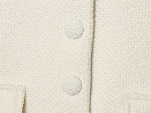Macro shot of cream bouclé tweed fabric texture with matching fabric-covered buttons