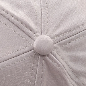 Macro shot of light gray satin baseball cap top with stitched panels and fabric button