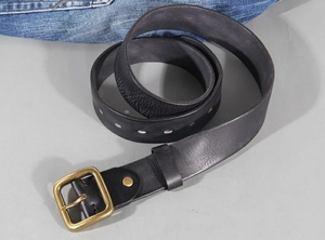 Macro view of vintage cowhide leather belt featuring a bronze pin buckle on blue jeans